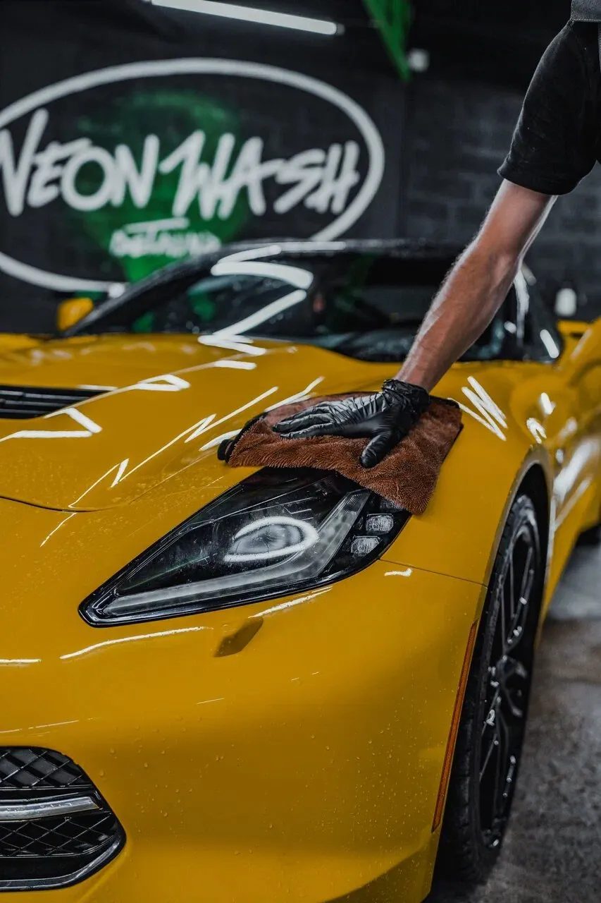 Мастер вытирает жёлтый Corvette микрофиброй на фоне логотипа Neon Wash